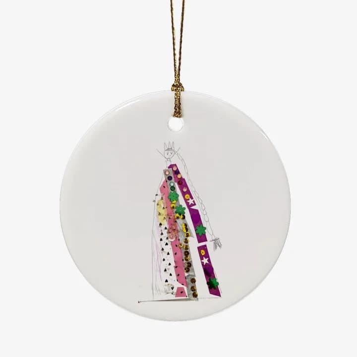 A mockup of the ceramic Christmas ornament: a child's drawing of a queen in a sequinned dress, exactly as drawn, on a round white ornament hanging from a gold string.